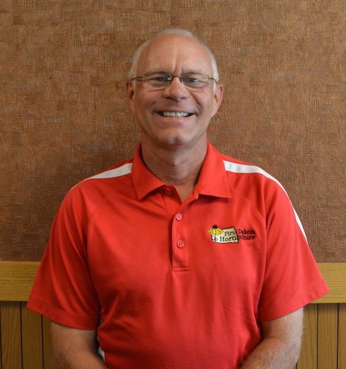 A man wearing glasses and a yellow shirt is smiling for the camera