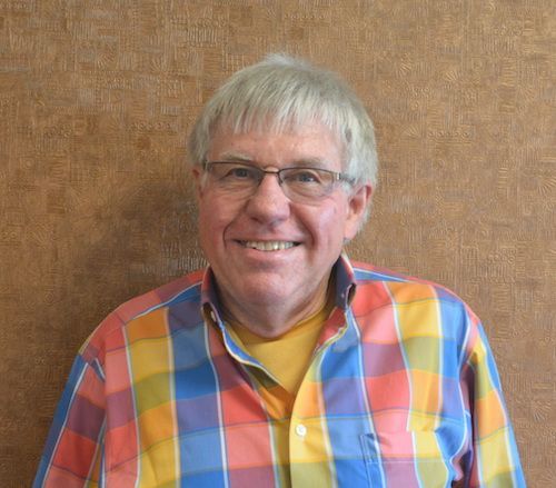 A man wearing glasses and a yellow shirt is smiling for the camera