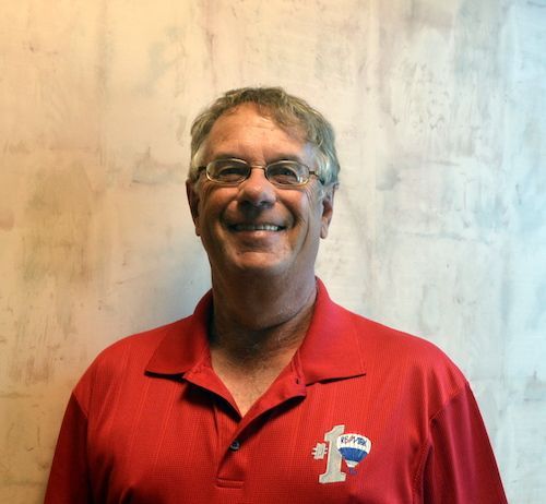 A man wearing glasses and a yellow shirt is smiling for the camera