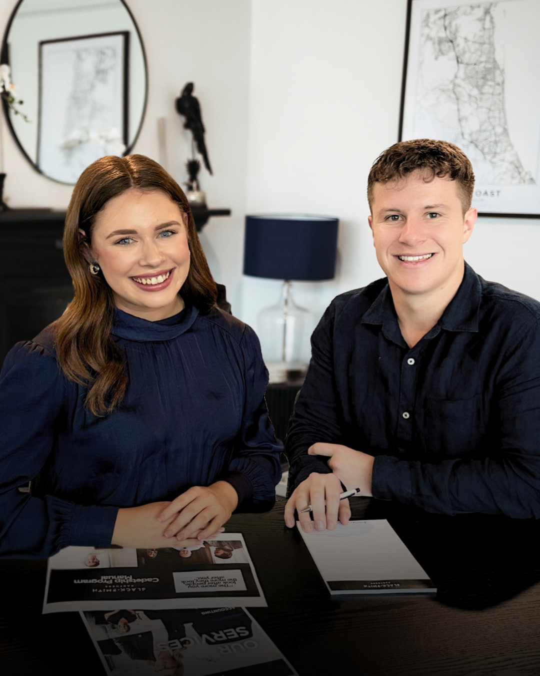 Woman and Man Smiling, Sitting at Table With Marketing Materials — Slack-Smith Partners in Tamworth, NSW
