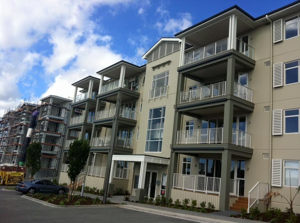 Apartment building with balconies and light beige exterior against a cloudy blue sky. Apartment building with balconies and light beige exterior against a cloudy blue sky.