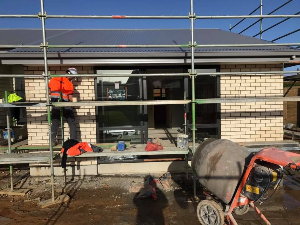 Construction worker on scaffolding, laying brick on a new building with a cement mixer in front. Construction worker on scaffolding, laying brick on a new building with a cement mixer in front.