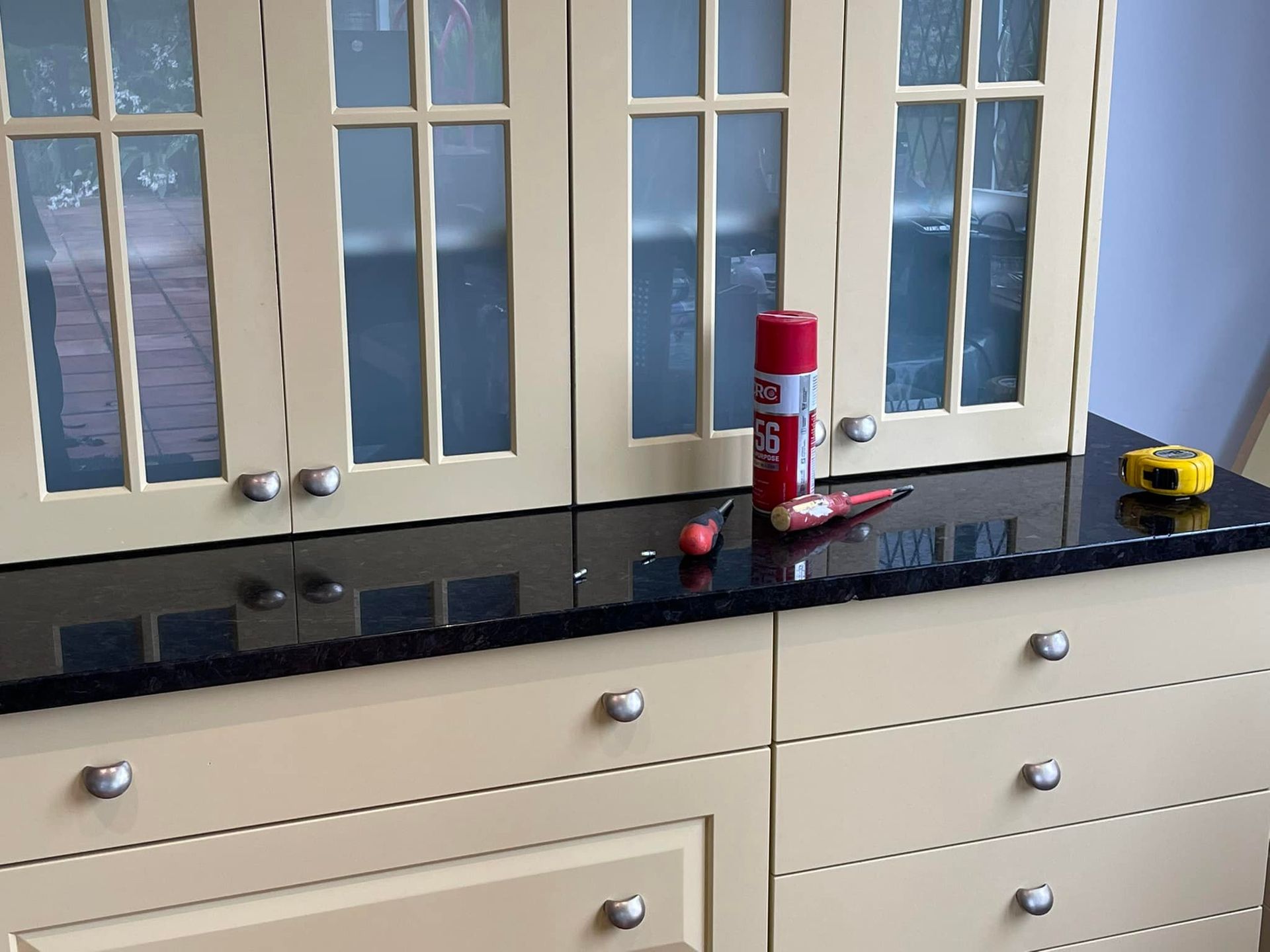 Kitchen cabinets with a black countertop and tools: spray paint, screwdriver, and tape measure. Kitchen cabinets with a black countertop and tools: spray paint, screwdriver, and tape measure.