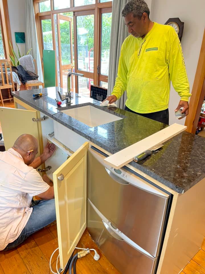 Two men installing a kitchen island with a granite countertop, and sink. One is working inside the cabinet. The other is looking on. Two men installing a kitchen island with a granite countertop, and sink. One is working inside the cabinet. The other is looking on.