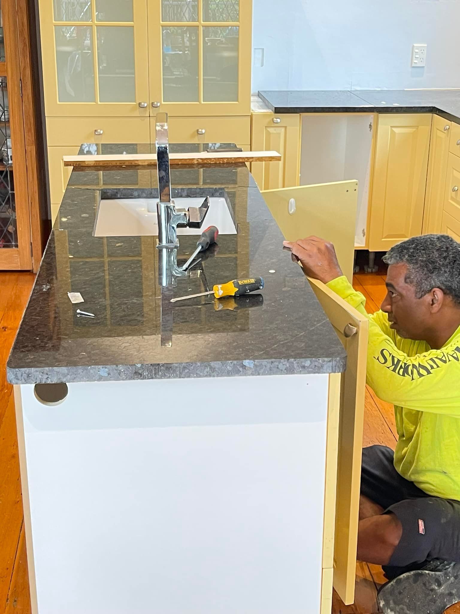 Person installing a cabinet door on a kitchen island with a granite countertop and a sink.