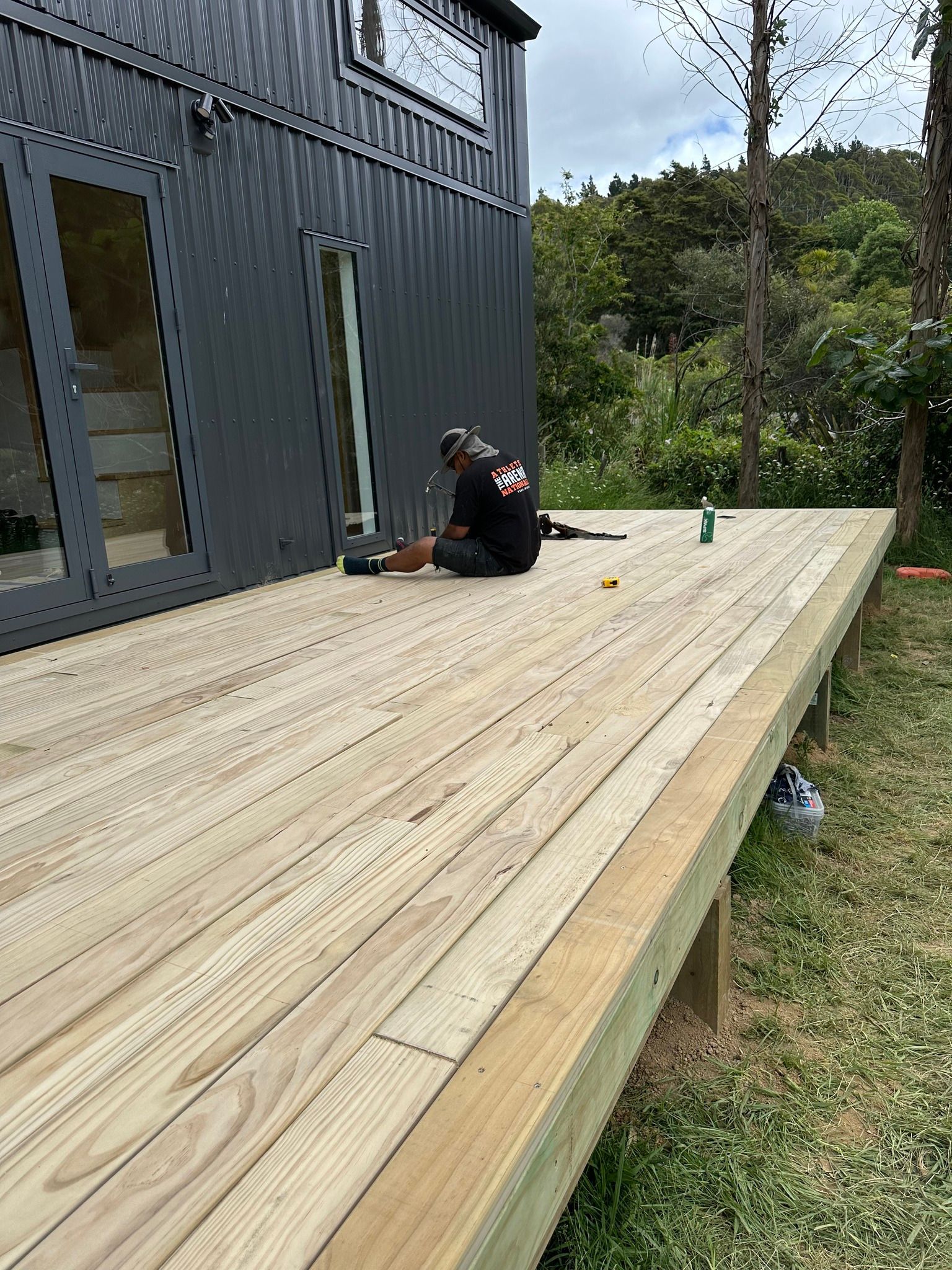 Person working on a wooden deck next to a dark gray house.