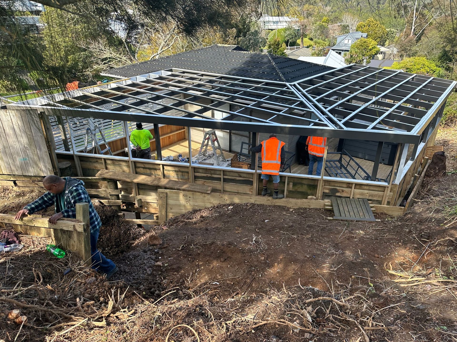 Construction of a building with workers on site, surrounded by foliage and a partially installed solar panel roof.