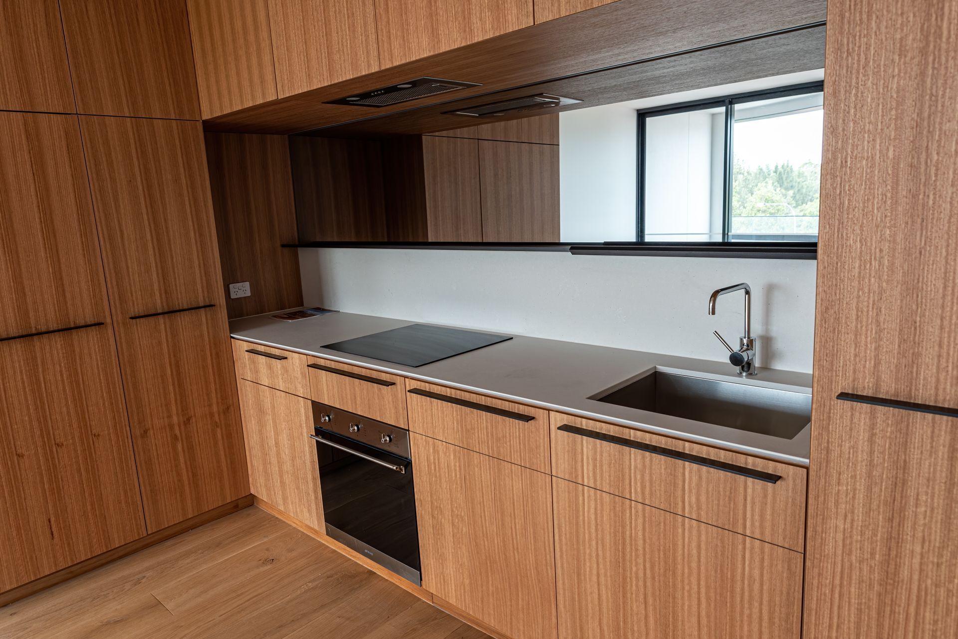 Modern kitchen with wood cabinets, gray countertop, black appliances, and a window. Modern kitchen with wood cabinets, gray countertop, black appliances, and a window.