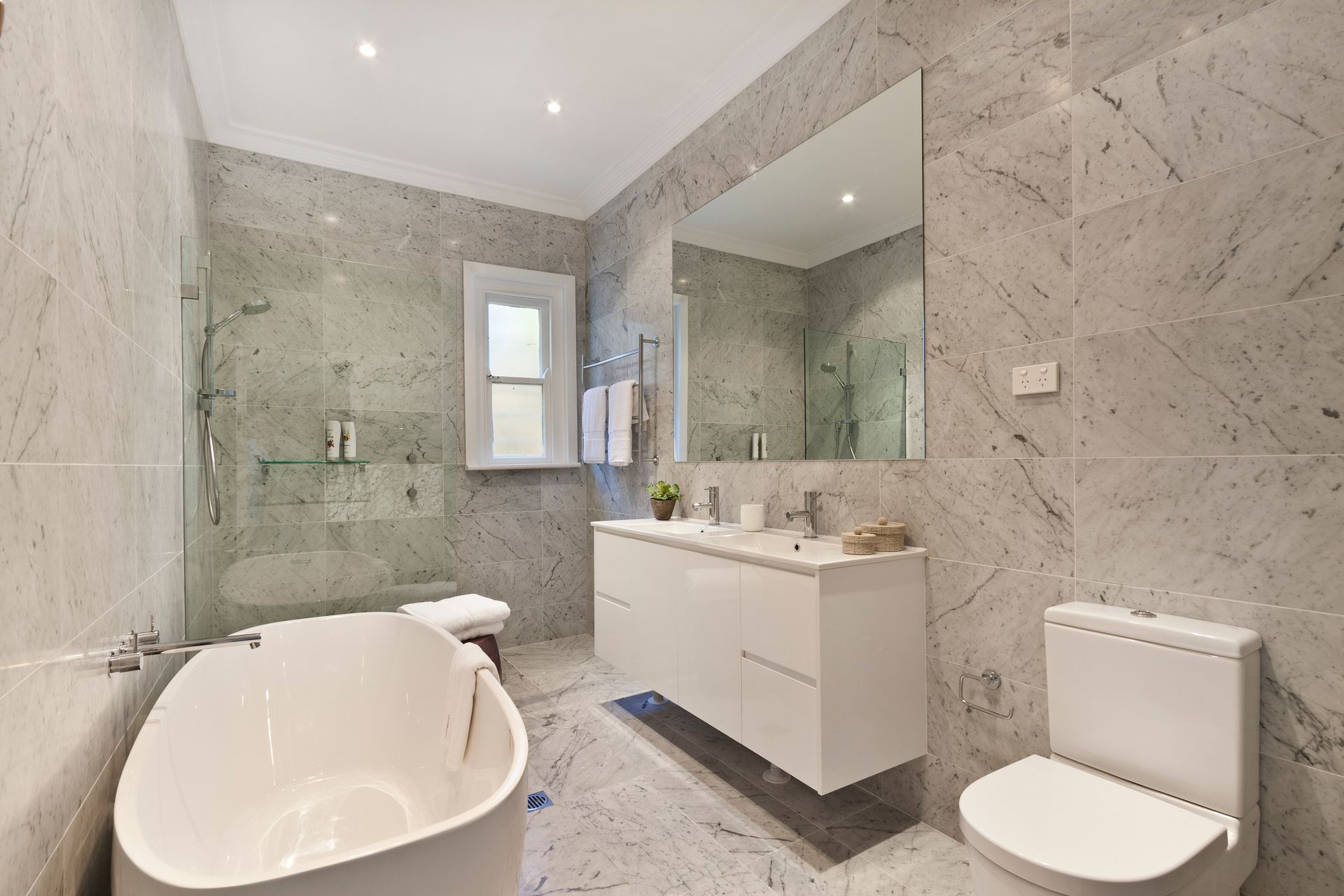 Modern bathroom with marble walls, soaking tub, floating vanity, and toilet. Modern bathroom with marble walls, soaking tub, floating vanity, and toilet.