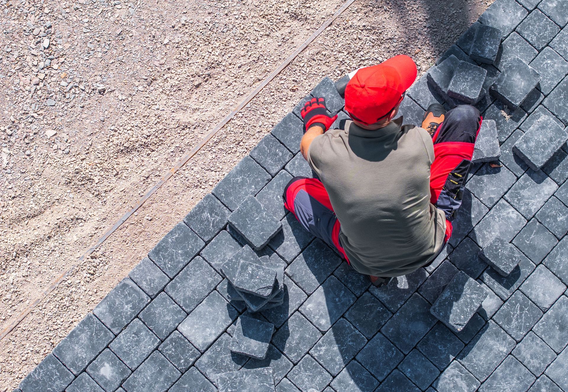 Construction worker, red hat and pants, laying gray paving stones. Construction worker, red hat and pants, laying gray paving stones.