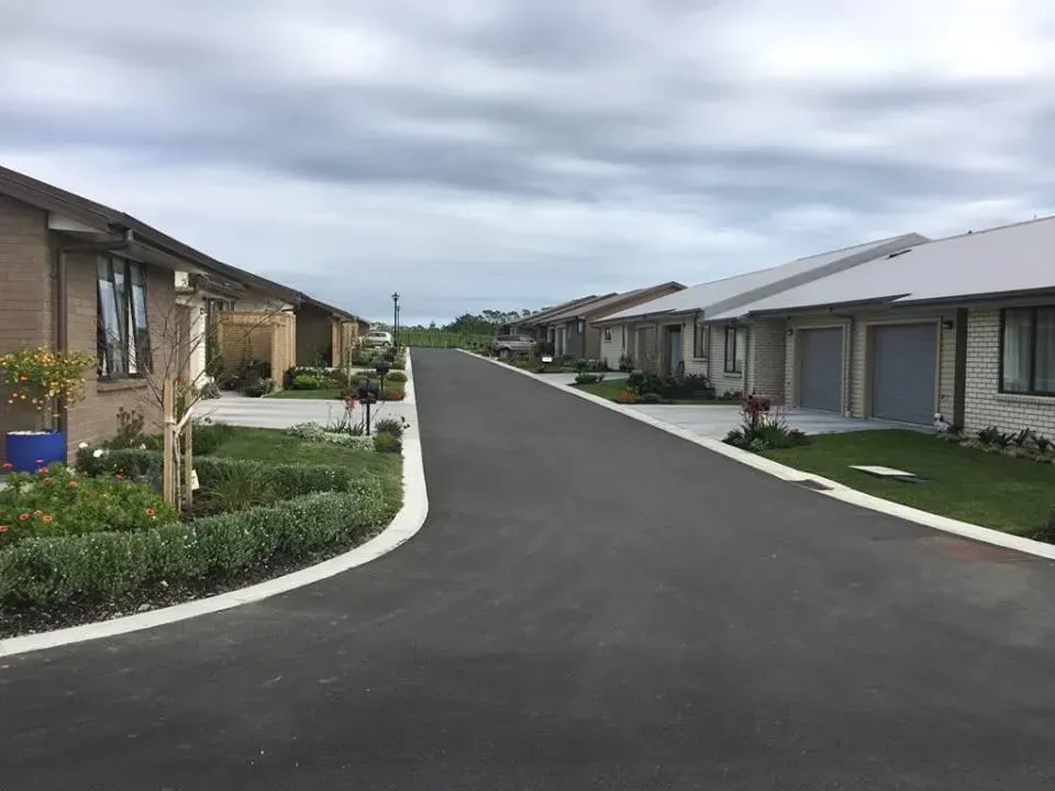 Row of suburban homes with a paved road and cloudy sky overhead.