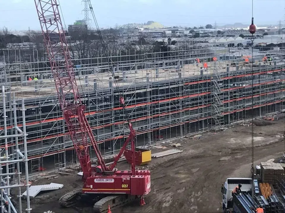 Construction site with red crane lifting materials to scaffolding structure.
