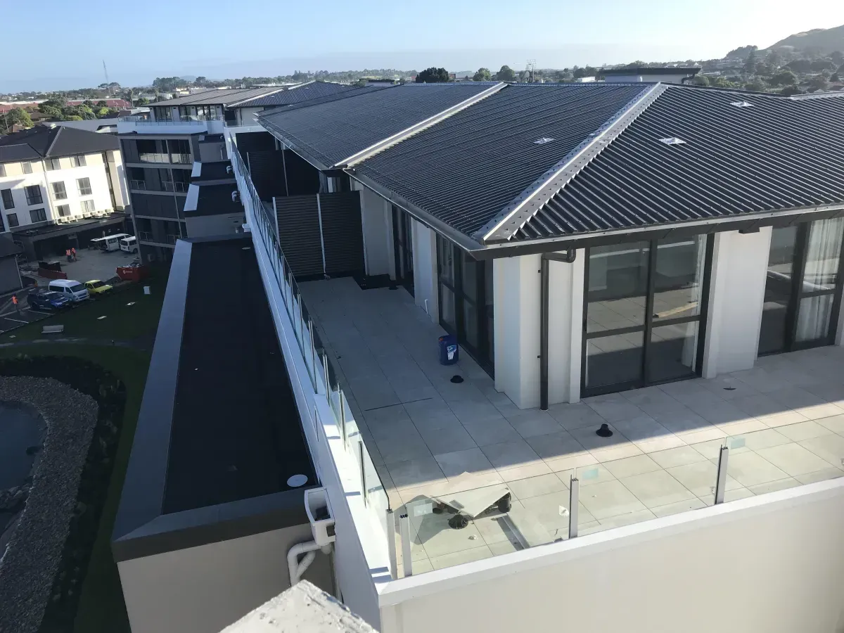 View from above of a building with a flat roof terrace and dark tiled roof in an urban setting.
