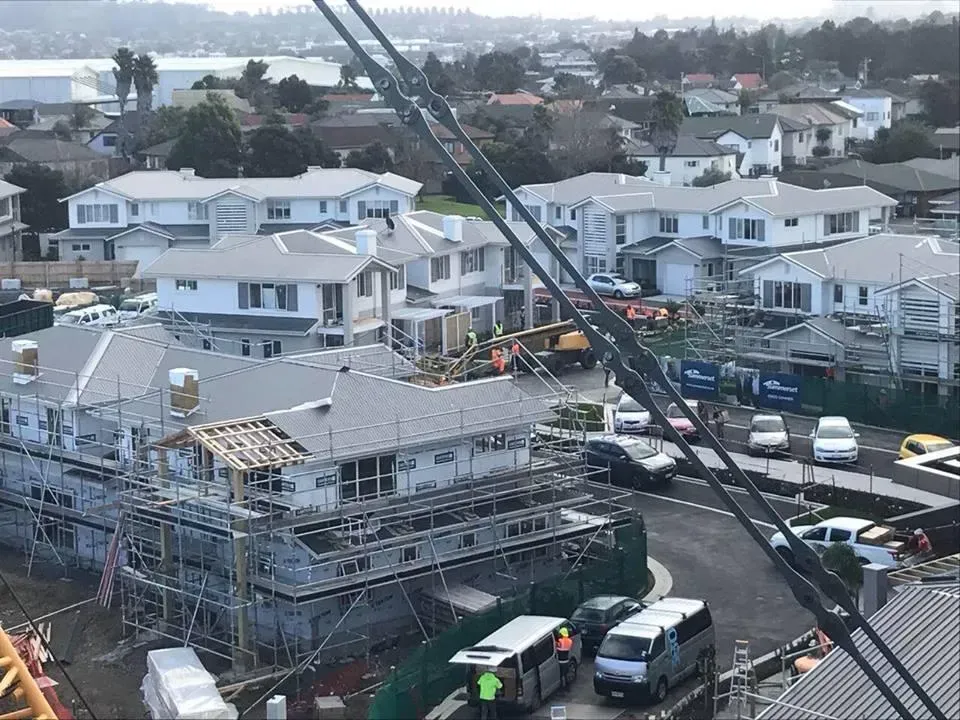 Construction site with buildings and scaffolding, vehicles, and a crane. Gray and white buildings in a residential area.