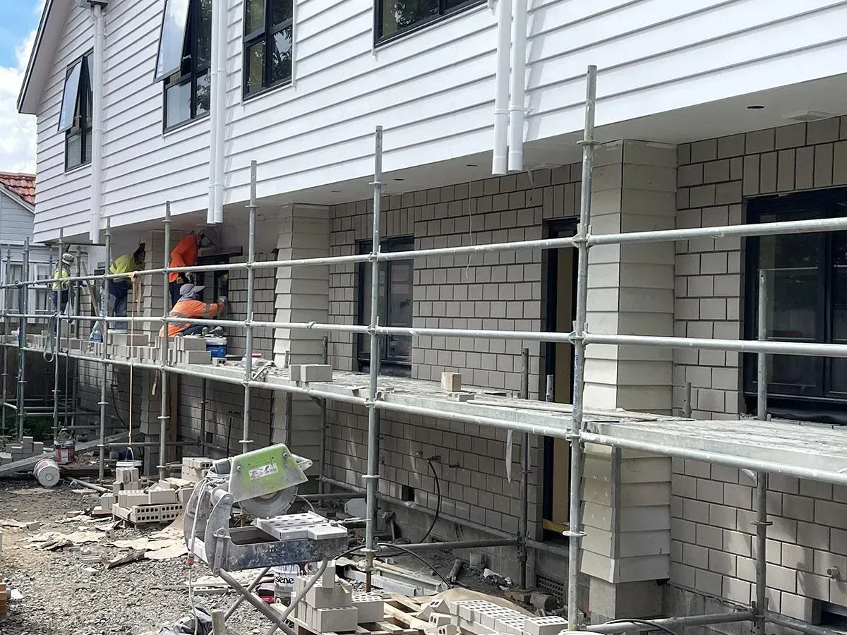 Construction site with scaffolding and workers applying brick veneer to a building.
