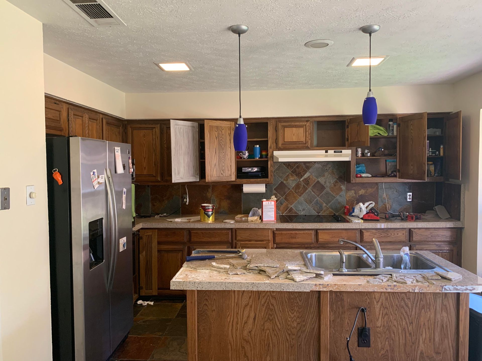 A kitchen with wooden cabinets , a stainless steel refrigerator , a sink , and a stove.