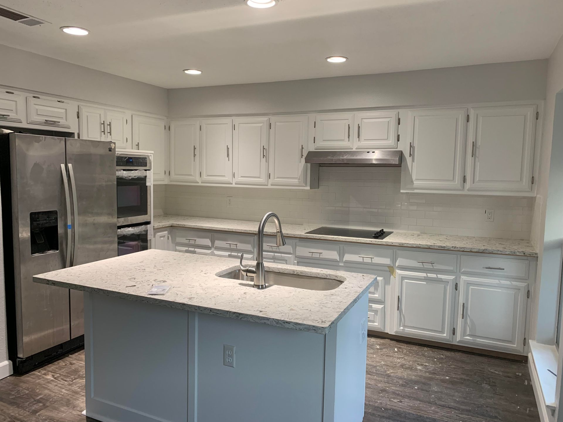 A kitchen with white cabinets , granite counter tops , stainless steel appliances and a large island.