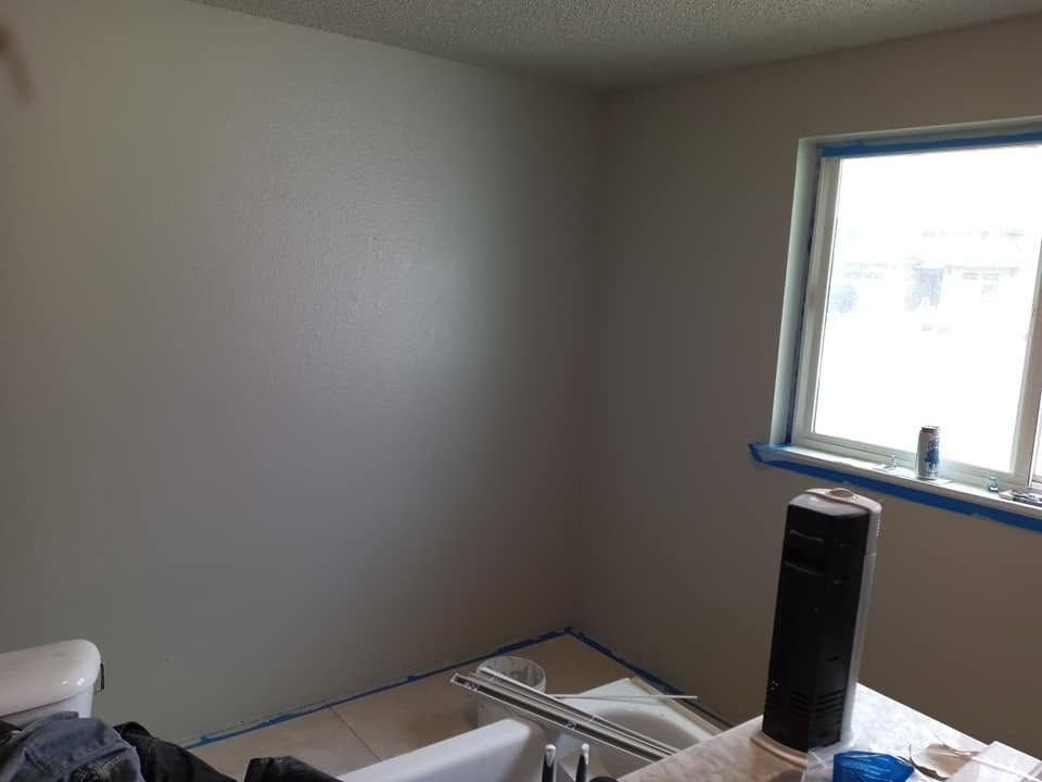 Empty room with beige walls, a window with blue tape, and a table holding tools and a black fan