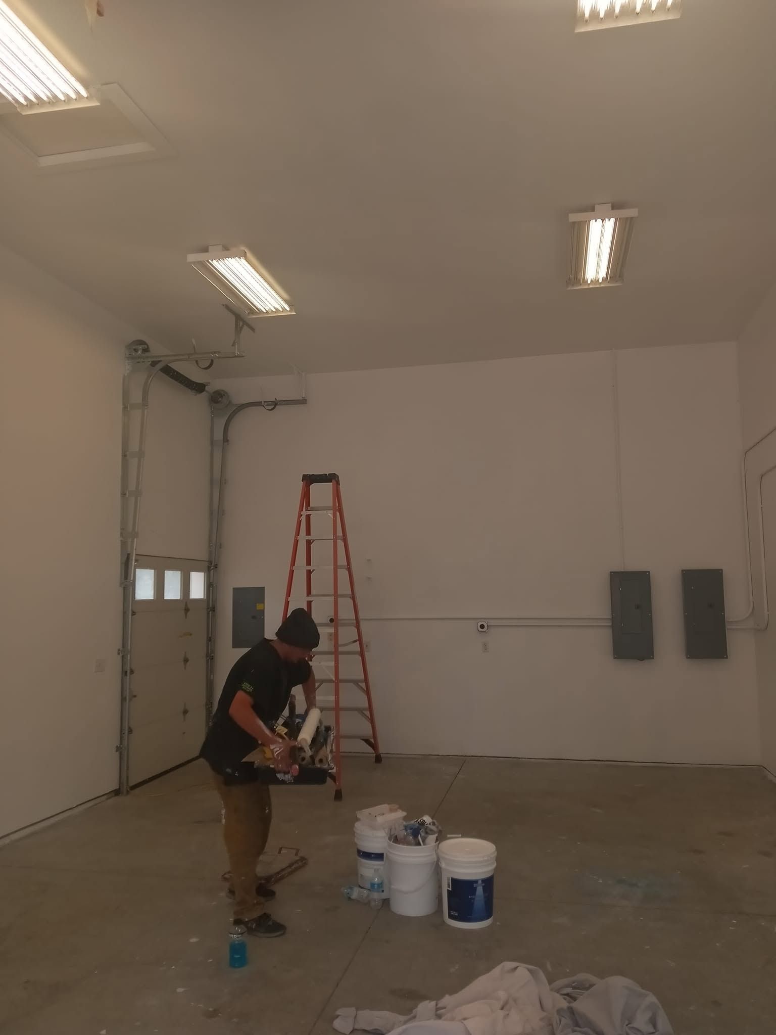 Person painting a large empty room with buckets and a ladder inside.