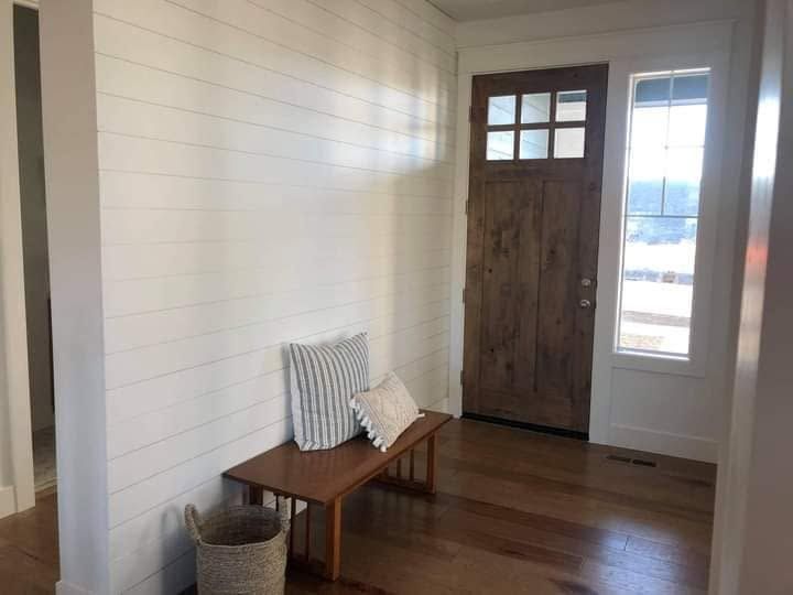 Bright entryway with white shiplap walls, wooden bench, wicker basket, and rustic front door.