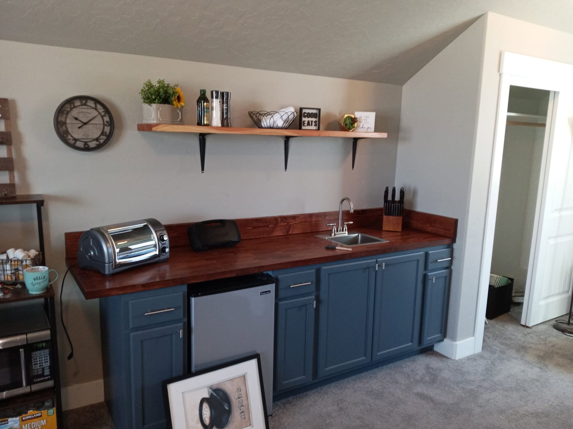 Home bar with blue cabinets, wood countertop, shelves, and a toaster oven against a wall