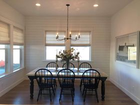 Bright dining room with a long table, black chairs, chandelier, and large windows along the walls