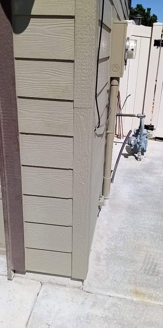 Side of a beige stucco building beside a concrete walkway, with a narrow gap and hanging cables.