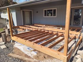 Porch floor under construction on a house, with exposed wooden joists and posts.