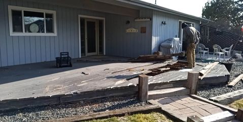 Person working on a damaged concrete patio beside a gray building and walkway demolition site