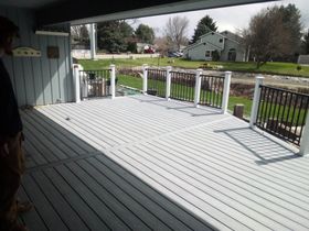 Covered porch with light gray decking and white railings overlooking a yard and street.
