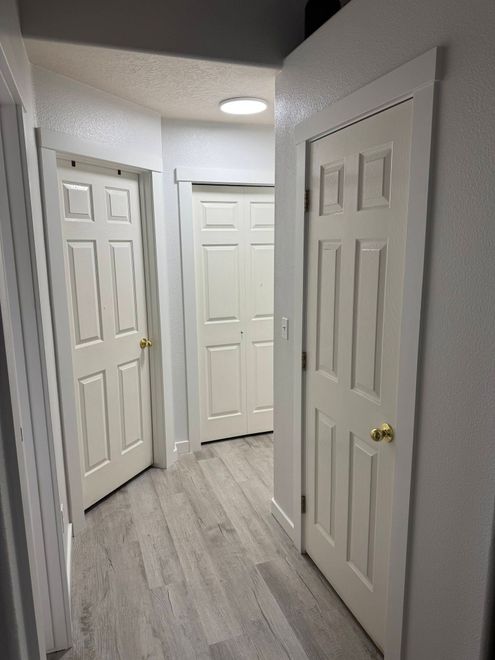 Narrow hallway with white doors, gray walls, and wood-look flooring, lit by ceiling lights
