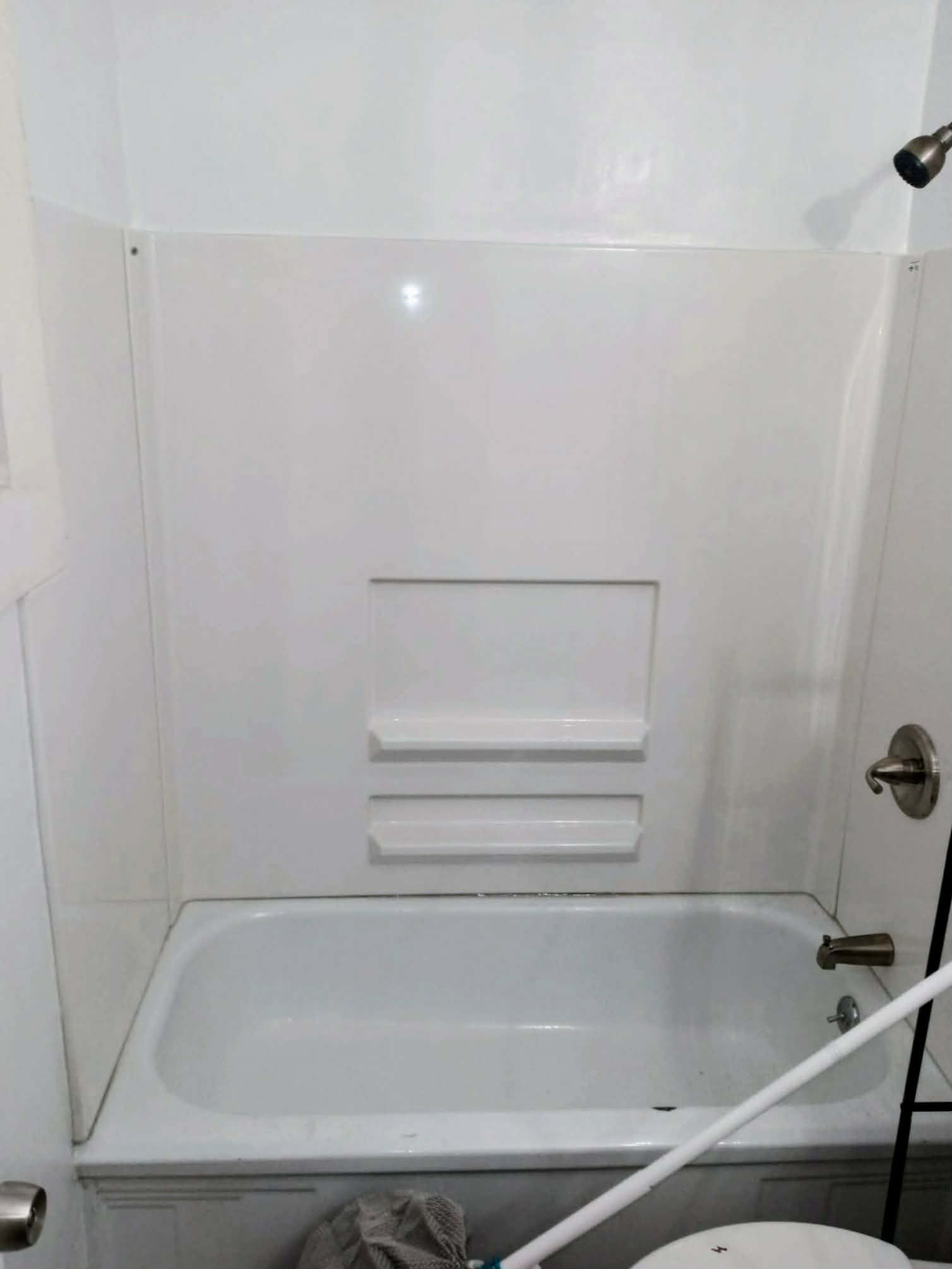 White tiled bathtub/shower alcove with a built-in soap shelf and chrome fixtures