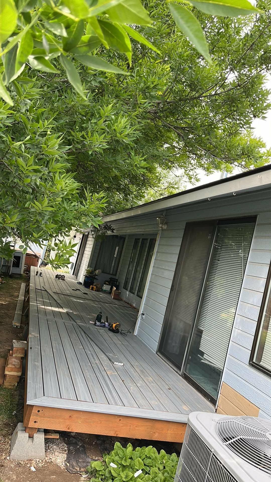 House with gray porch under leafy tree canopy, viewed from the side.