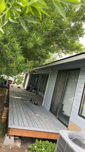 Gray porch of a house under green tree branches, with sliding doors and a small air conditioner unit visible.