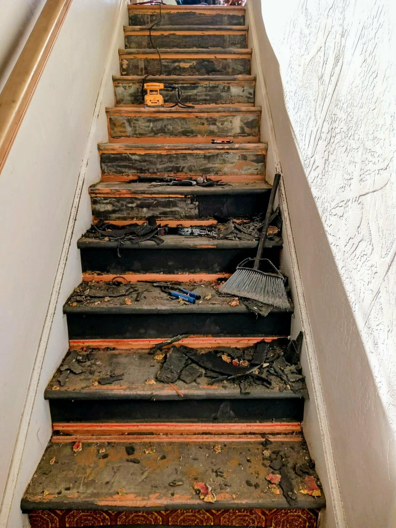 Burned, debris-covered staircase inside a damaged building, with charred steps and soot-stained walls