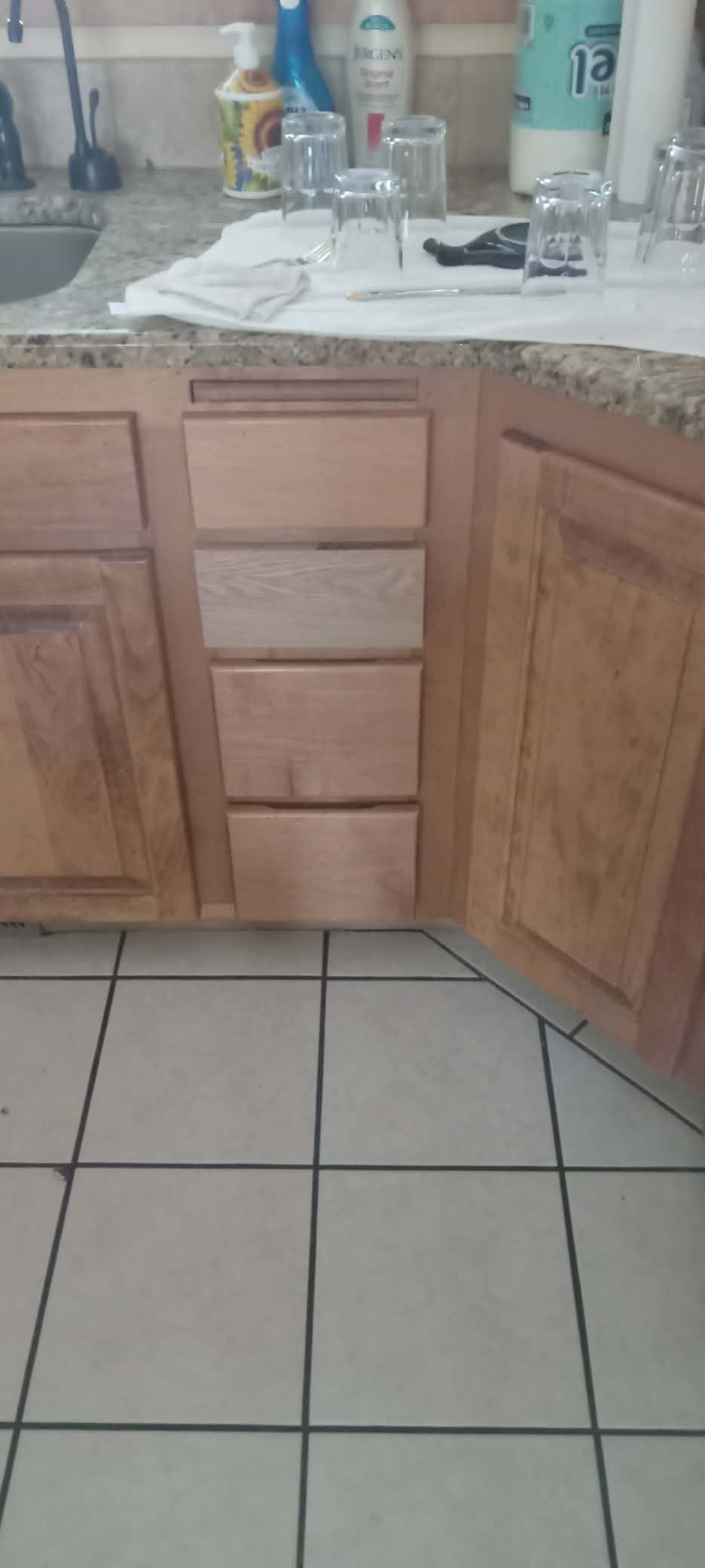 Kitchen sink cabinet with a granite countertop, tiled floor, and items on the counter