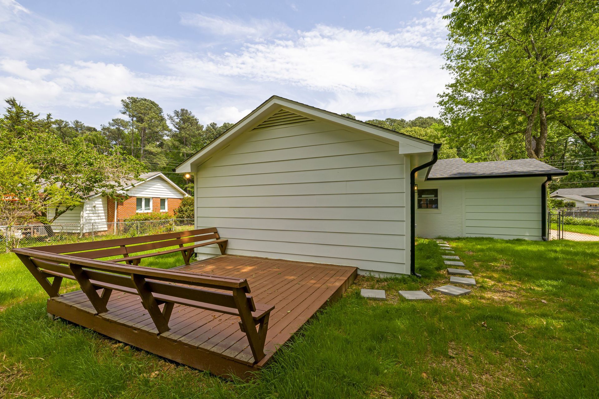 Backyard deck with wooden picnic table beside a white shed and green lawn under a cloudy sky