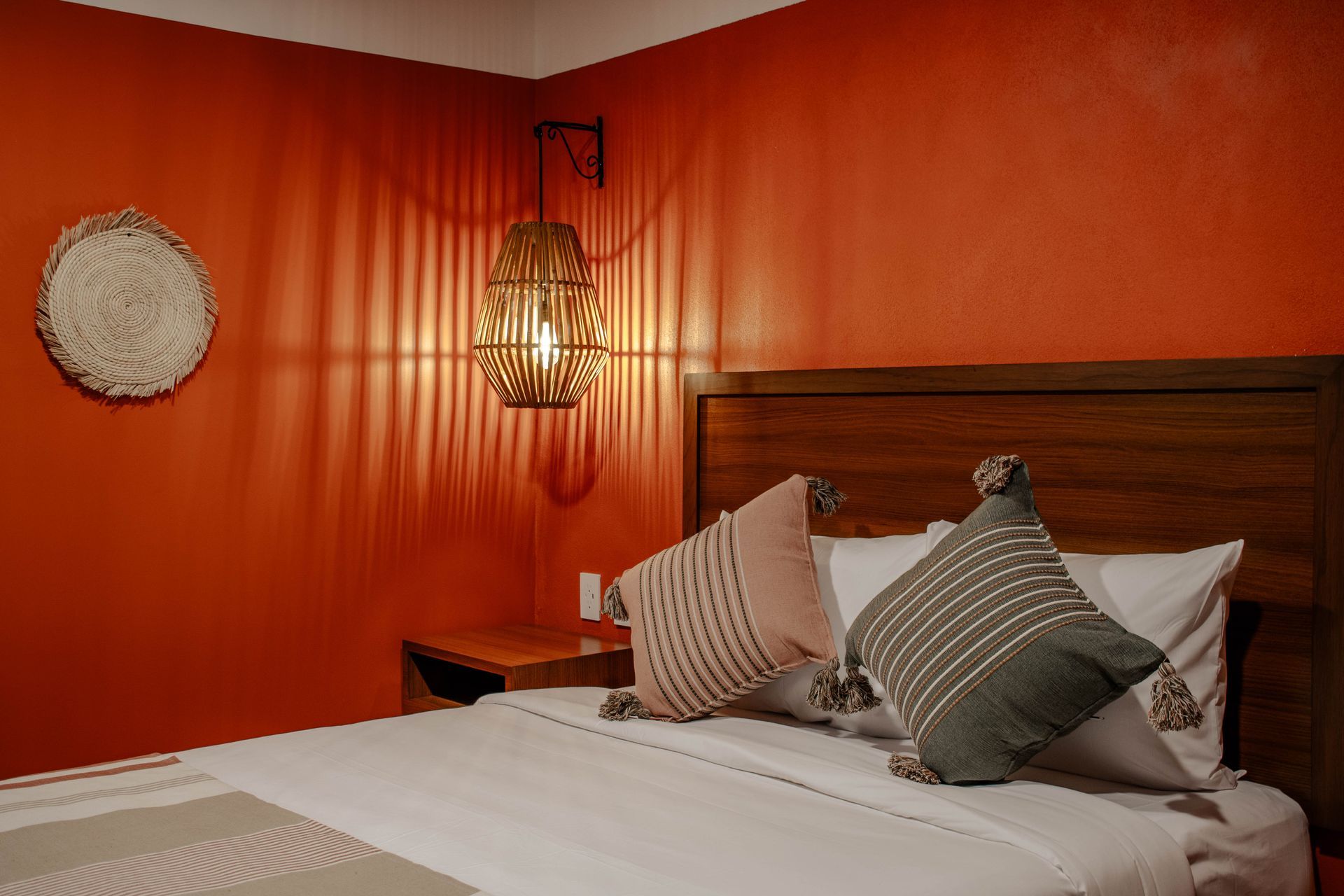 Dormitorio con paredes naranjas, cama de madera, cojines a rayas y una lámpara colgante