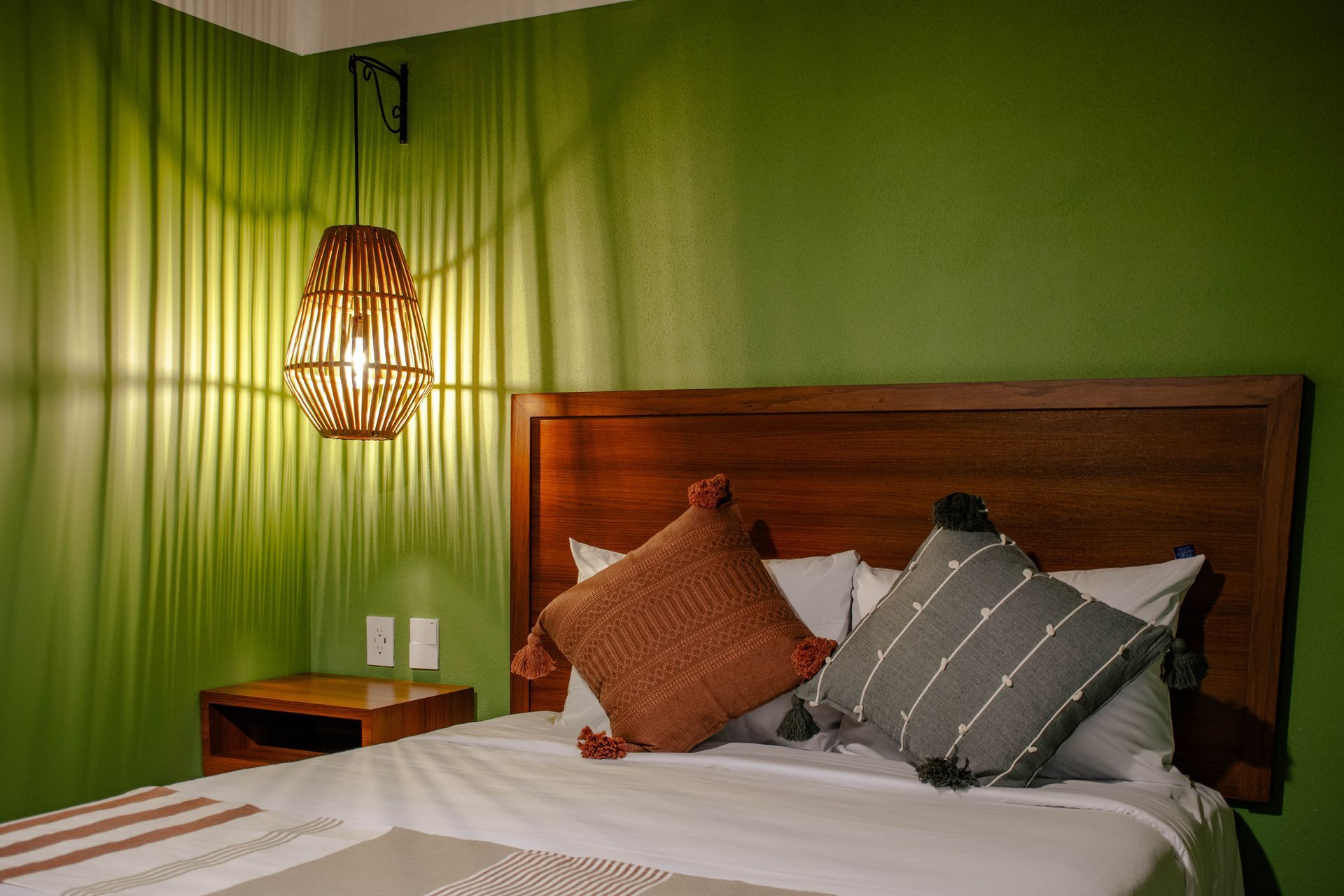 Dormitorio con paredes verdes, cabecero de madera, ropa de cama blanca y la cálida luz de una lámpara colgante