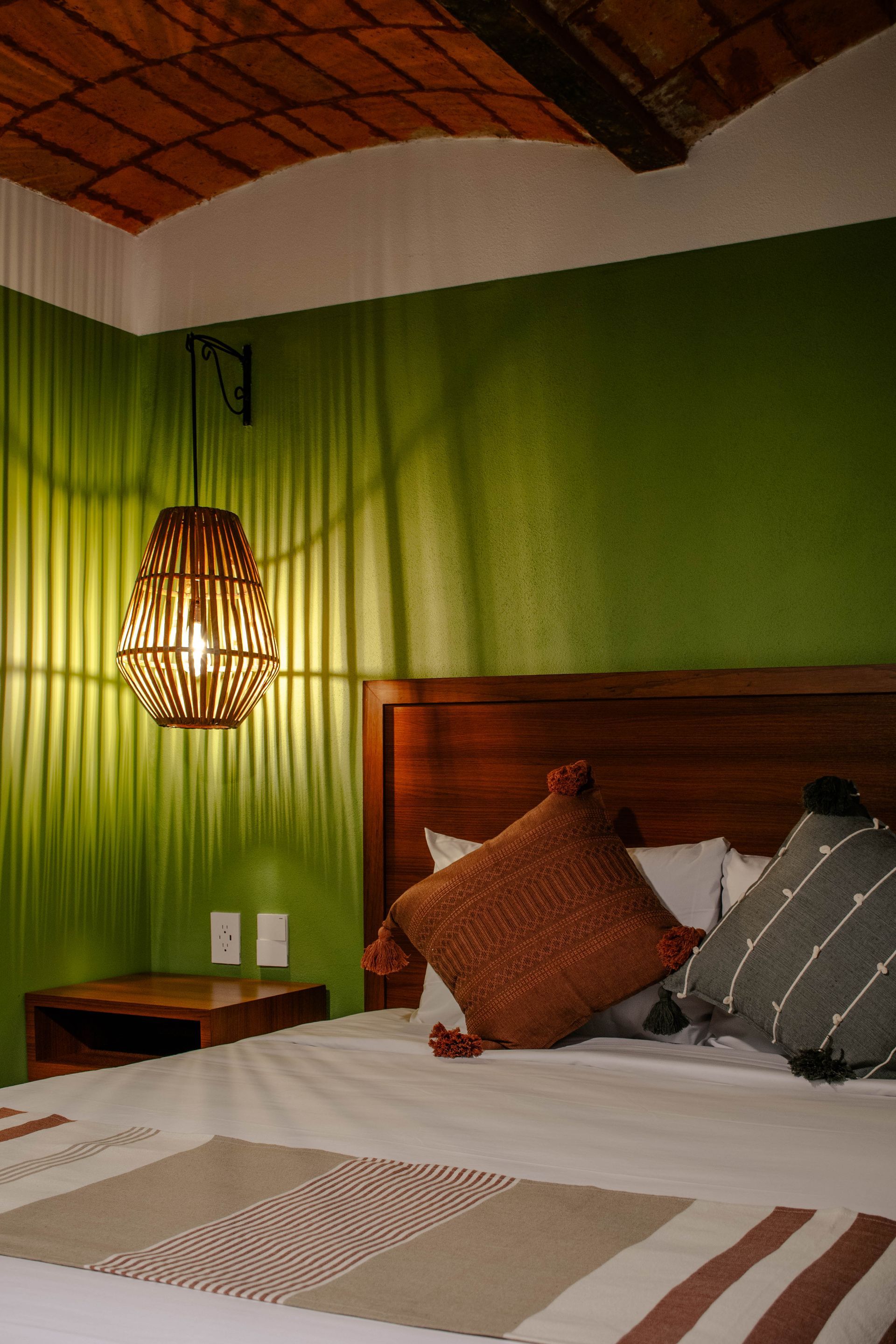 Acogedor dormitorio con paredes verdes, cabecero de madera, lámpara colgante de mimbre y cama con cojines estampados
