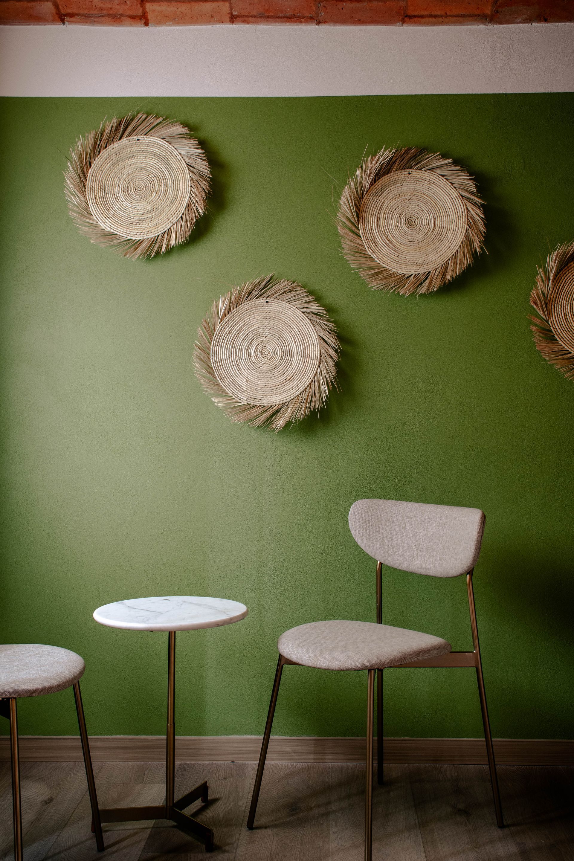 Pared verde con adornos de paja sobre dos sillas blancas de cafetería y una mesita redonda