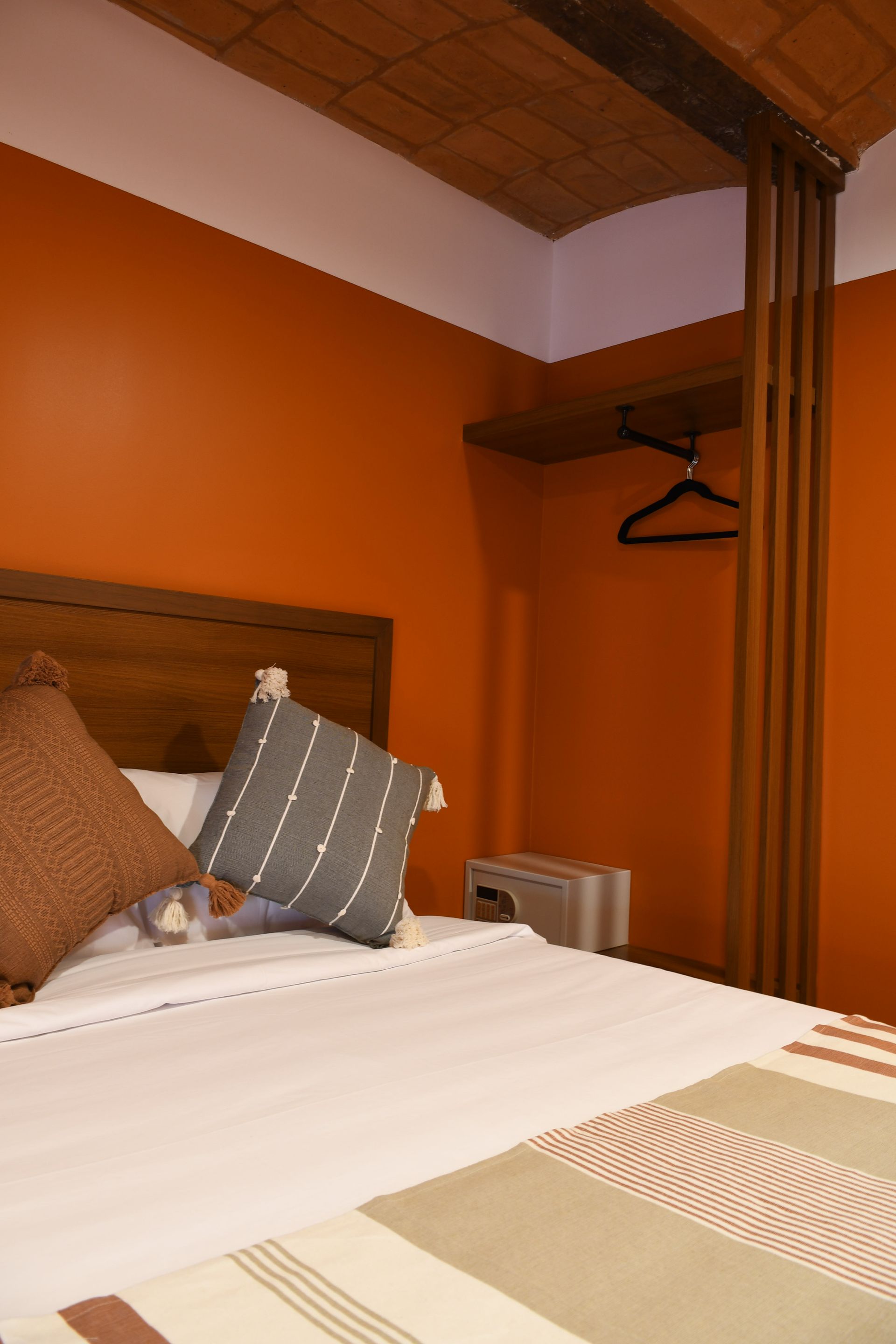 Dormitorio naranja con cama, cojines a rayas, techo de madera y ganchos en la pared con una prenda colgada