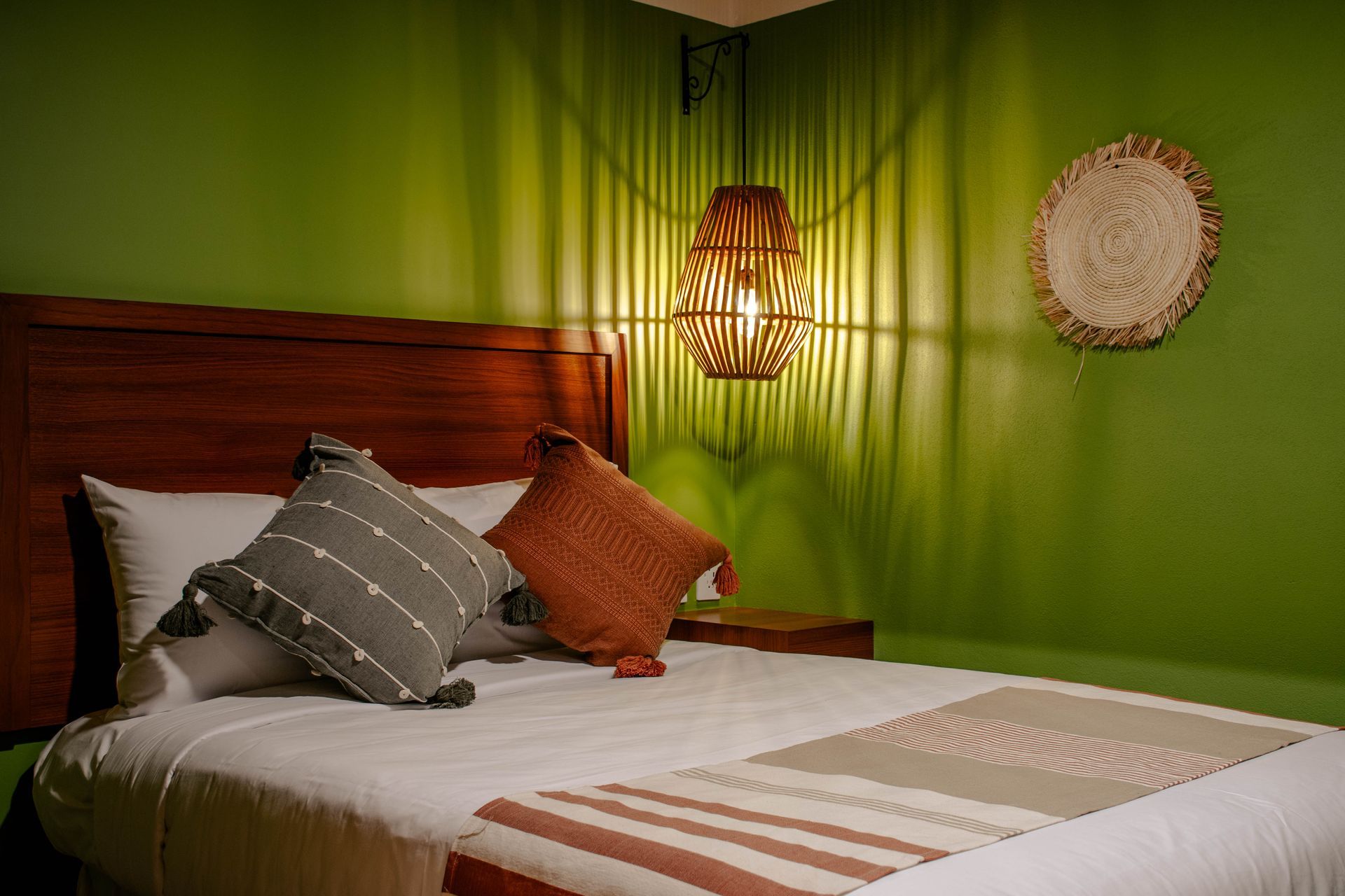 Dormitorio acogedor con paredes verdes, cabecero de madera, colcha blanca y una lámpara colgante que ilumina la habitación