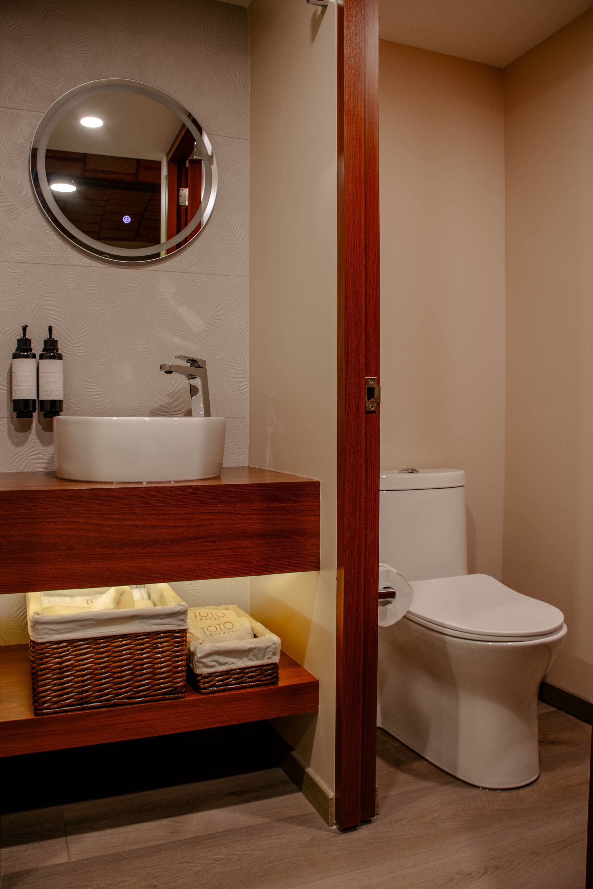 Baño pequeño con lavabo, espejo, inodoro y estante de madera para el tocador en tonos beige