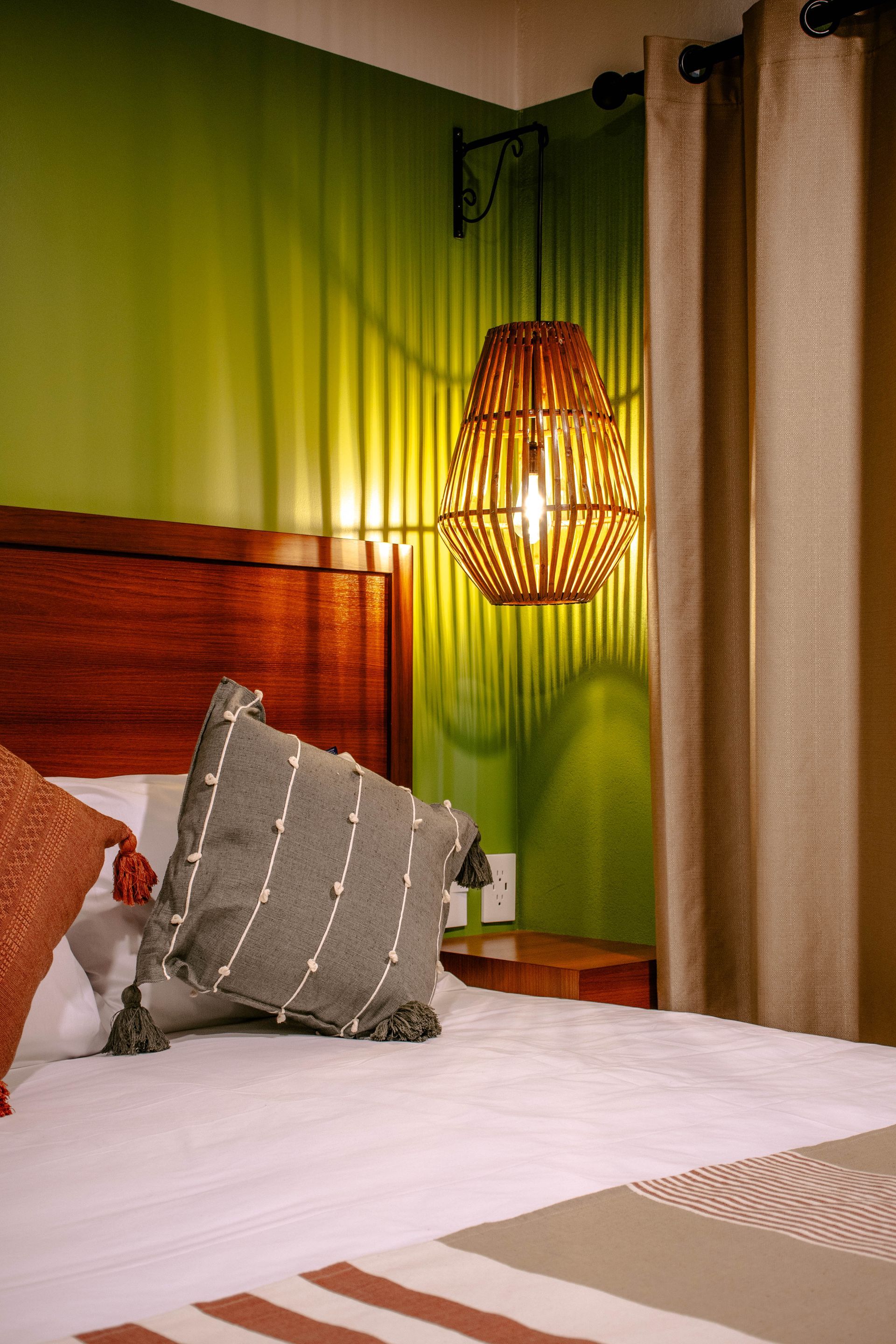 Dormitorio acogedor con cama blanca, almohadas grises, cabecero de madera, pared verde y lámpara colgante de mimbre