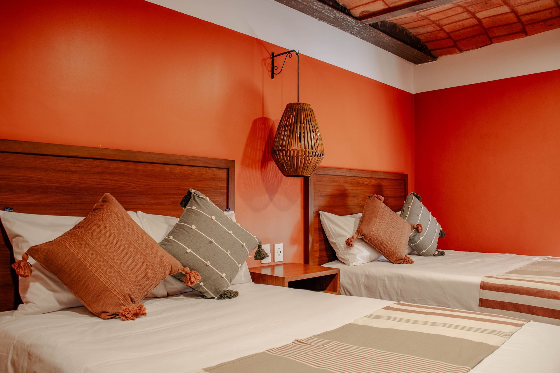 Dos camas en un dormitorio de tonos cálidos anaranjados, con cabeceros de madera y almohadas estampadas