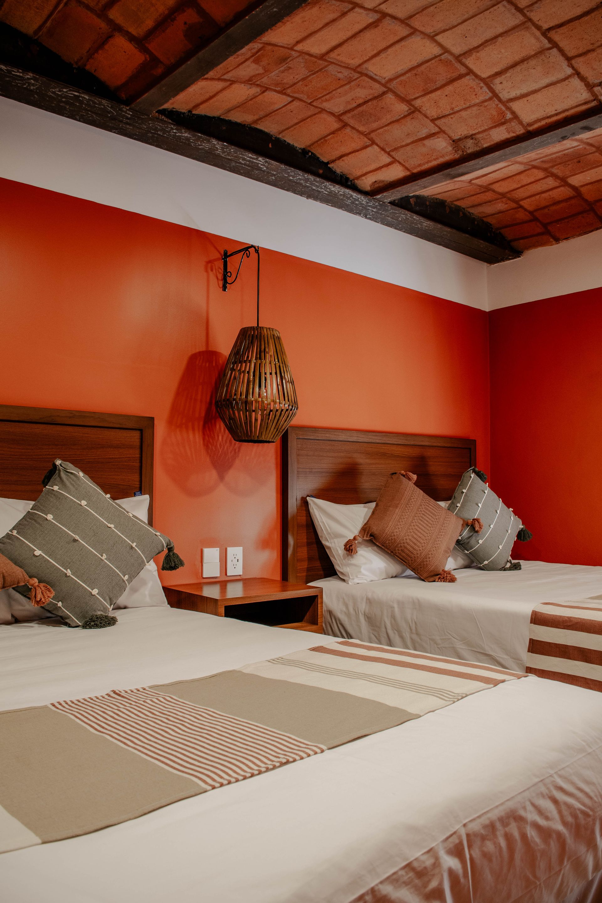 Acogedor dormitorio naranja con dos camas individuales, cojines estampados y techo de terracota
