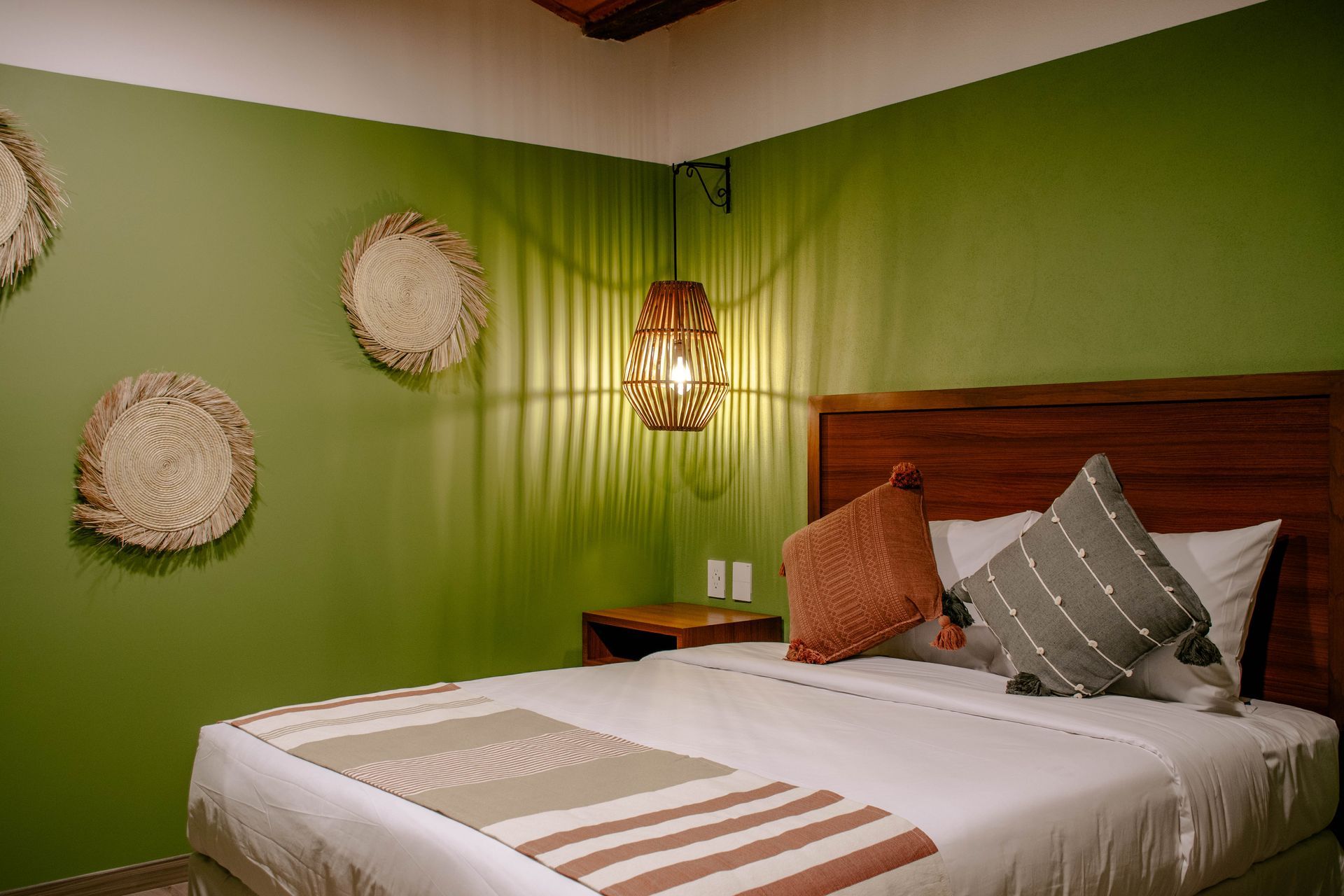 Dormitorio acogedor con paredes verdes, cama de madera, decoración de pared tejida y una cálida lámpara colgante