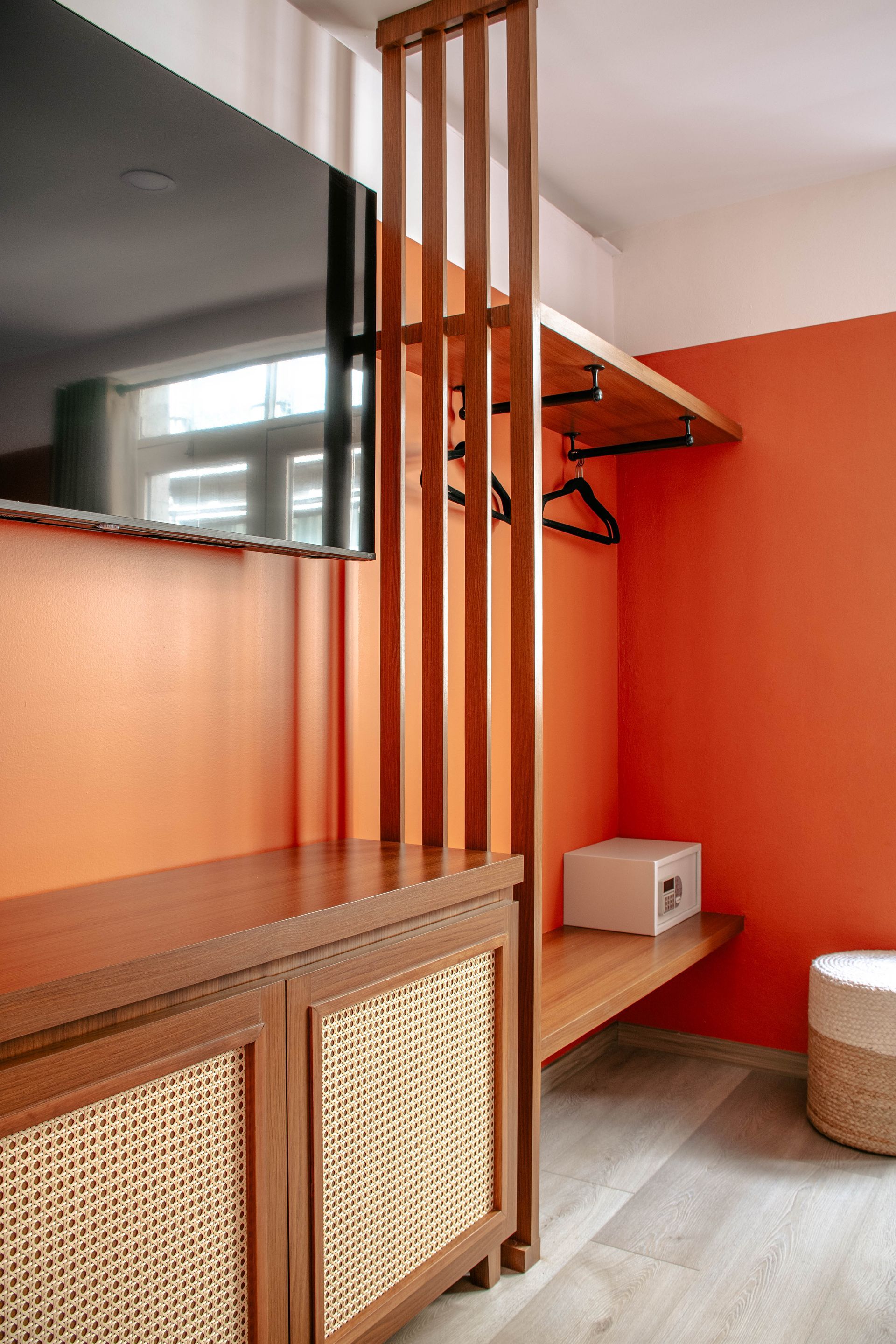 Habitación de hotel moderna con listones de madera, televisor colgado en la pared, pared de acento naranja y armario abierto