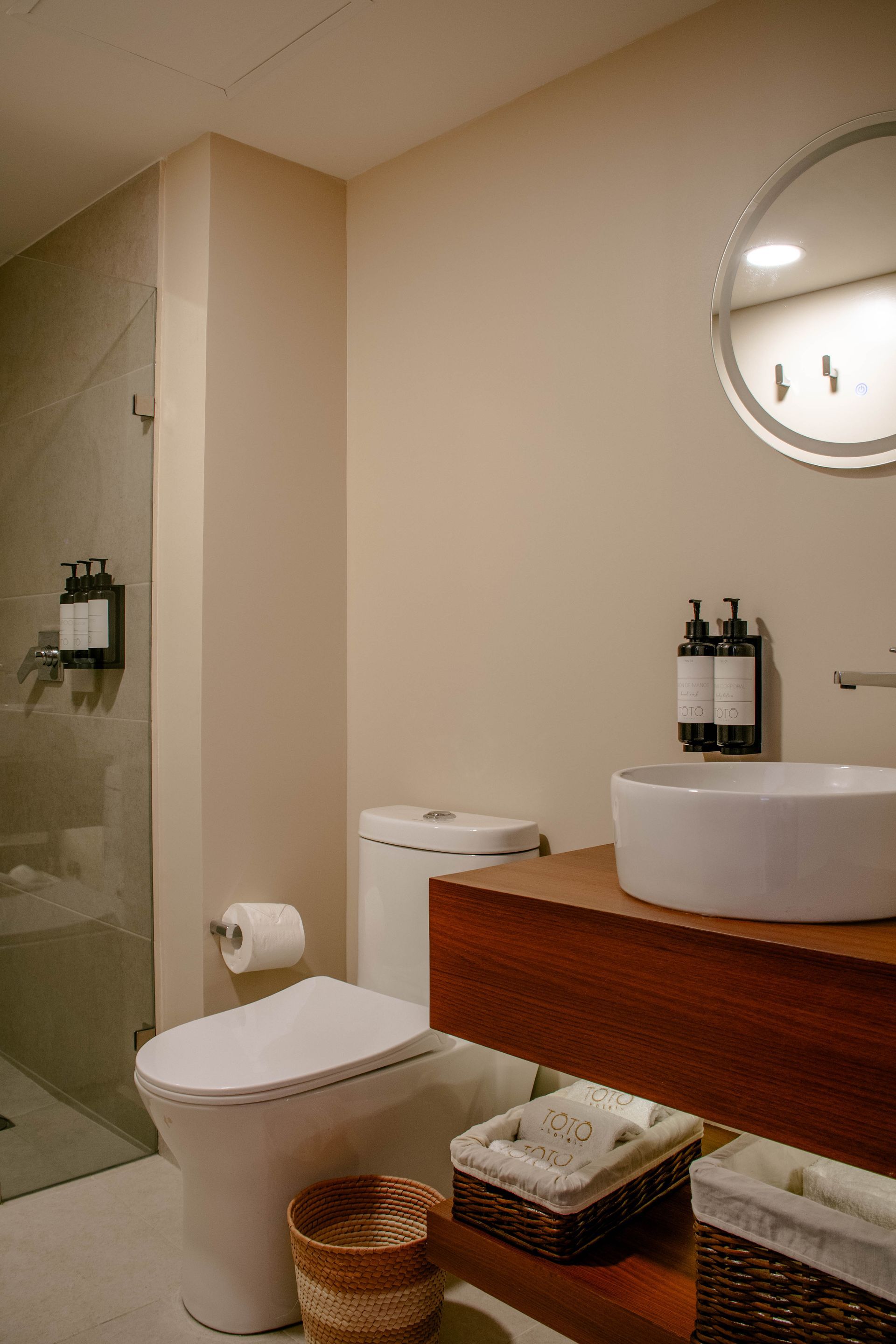 Baño moderno con inodoro, tocador de madera, lavabo, espejo y mampara de ducha de cristal